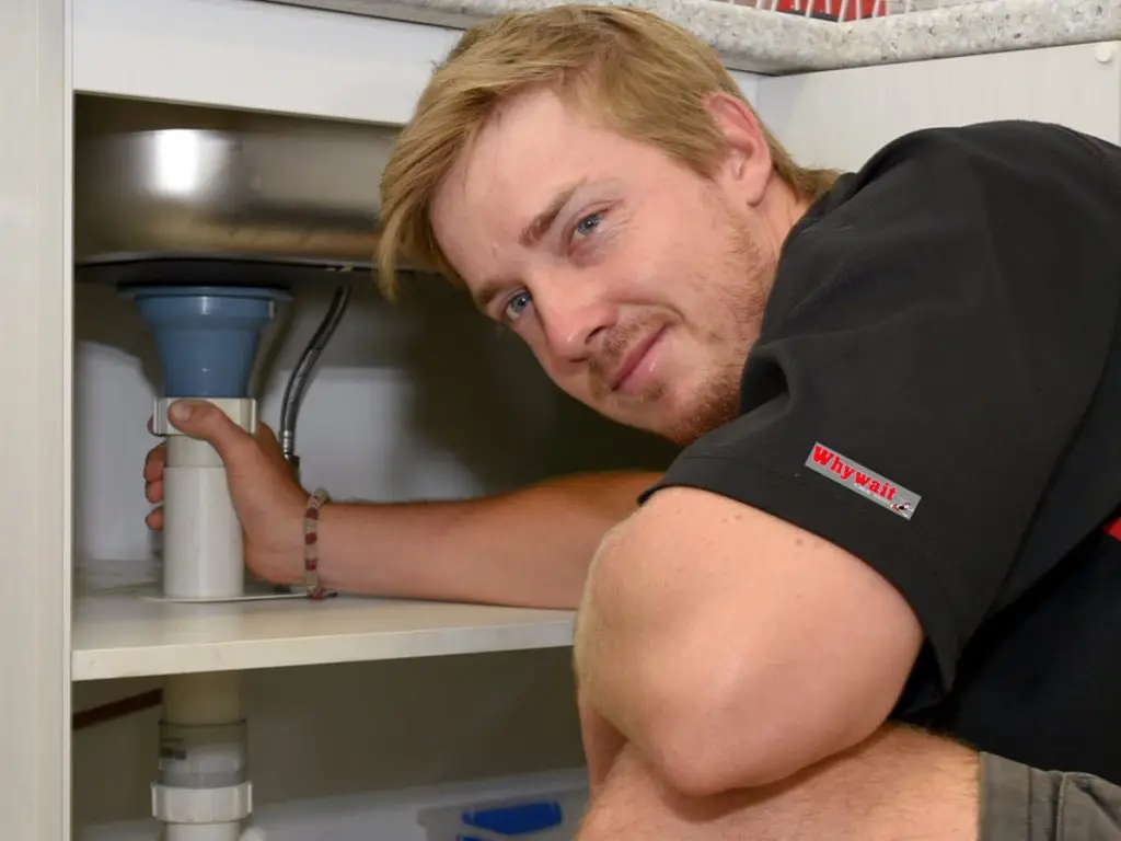 Plumber installing auto flood stop valve under kitchen sink
